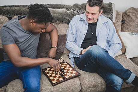 A multi ethnic gay couple spending an enjoyable time at home on the sofa playing chess with each other.